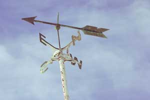 A sign on a pole showing the 4 cardinal points with an arrow on top that shows the direction of the wind