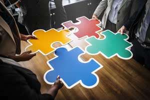 4 people standing around a table, putting together a puzzle of 4 pieces